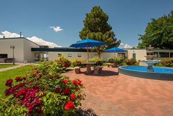 a courtyard with flowers and a fountain and a building in the background